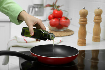 Woman pouring cooking oil from bottle into frying pan in kitchen, closeup - obrazy, fototapety, plakaty
