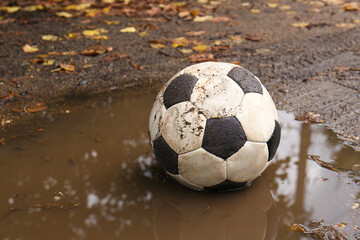 Dirty soccer ball in muddy puddle, space for text