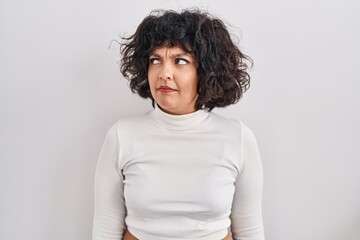 Hispanic woman with curly hair standing over isolated background smiling looking to the side and staring away thinking.