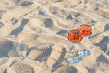 Glasses of tasty rose wine on sand, space for text
