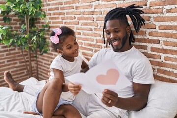 Father and daughter sitting on bed reading lovely message at bedroom