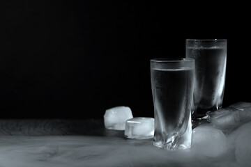 Vodka in shot glasses with ice on table against black background, space for text