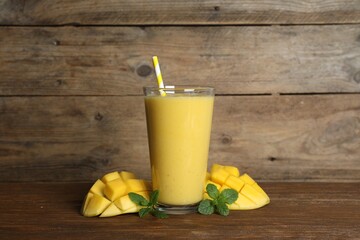 Glass of tasty smoothie with straw, mint leaves and mango on wooden table
