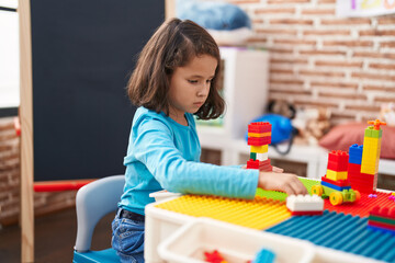 Adorable chinese girl playing with construction blocks sitting on table at kindergarten