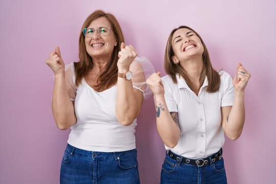 Hispanic mother and daughter wearing casual white t shirt over pink background celebrating surprised and amazed for success with arms raised and eyes closed. winner concept.