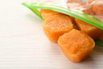 Frozen nectarine puree cubes in plastic bag on white wooden table, closeup. Space for text