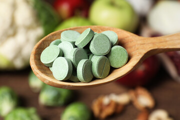 Wooden spoon of pills over table with foodstuff, closeup. Prebiotic supplements