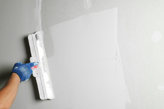 Professional worker plastering wall with putty knife, closeup