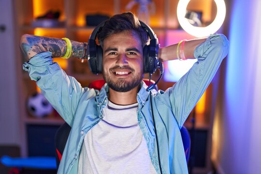 Young hispanic man streamer smiling confident relaxed with hands on head at gaming room