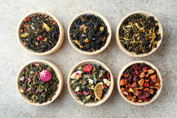 Different kinds of dry herbal tea in wooden bowls on light grey table, flat lay