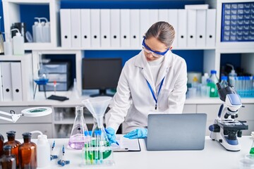 Young woman scientist writing on clipboard at laboratory