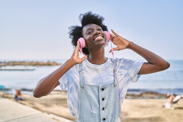 Young african woman listening to music using headphones by the sea