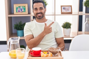 Fototapeta na wymiar Hispanic man with beard eating breakfast smiling cheerful pointing with hand and finger up to the side