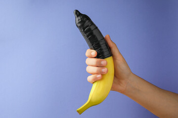 Woman holding banana in condom on light blue background, closeup and space for text. Safe sex...