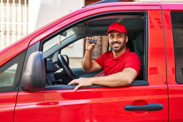 Fototapeta na wymiar Young hispanic man courier holding key sitting on car at street