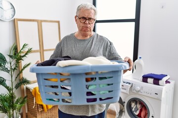 Senior caucasian man holding detergent bottle at laundry room depressed and worry for distress, crying angry and afraid. sad expression.