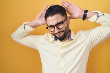 Hispanic young man wearing business clothes and glasses doing bunny ears gesture with hands palms looking cynical and skeptical. easter rabbit concept.