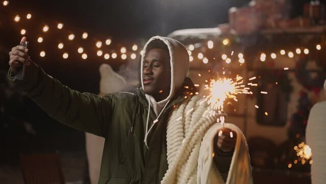 african american man is taking selfie with sparkler on Christmas market in square