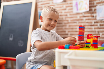 Adorable toddler playing with construction blocks sitting on table at classroom