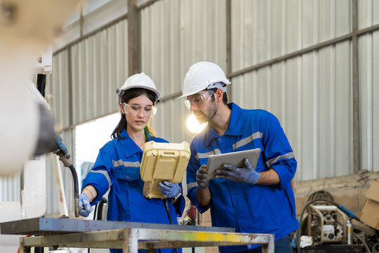 Two male and female engineer working with robot arm system welding at production plant factory. Engineer worker checking and maintenance robot arm system welding