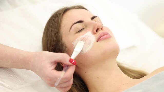 Young woman during peeling treatment in beauty clinic. Attractive woman in cosmetology studio.