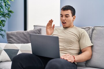 Young arab man using laptop at home scared and amazed with open mouth for surprise, disbelief face