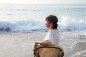 Fototapeta premium Happy woman sitting chair near the sea waves and enjoying the sea view.