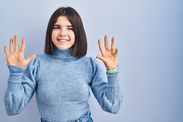 Young hispanic woman standing over blue background showing and pointing up with fingers number nine while smiling confident and happy.