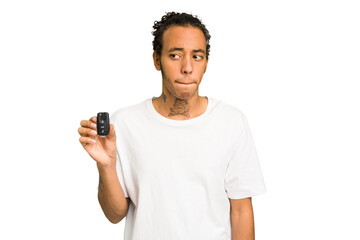 Young African American man holding car keys isolated confused, feels doubtful and unsure.