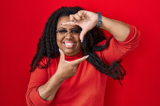 Plus size hispanic woman standing over red background smiling making frame with hands and fingers with happy face. creativity and photography concept.