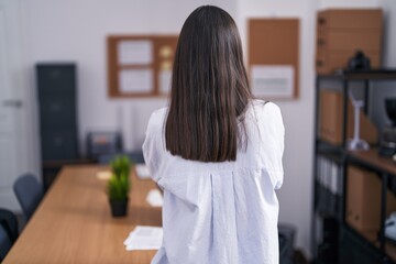 Young hispanic woman at the office standing backwards looking away with crossed arms