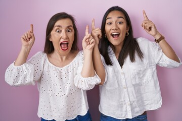 Hispanic mother and daughter together smiling amazed and surprised and pointing up with fingers and raised arms.