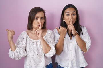 Hispanic mother and daughter together asking to be quiet with finger on lips pointing with hand to...