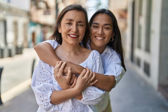 Two women mother and daughter smiling confident hugging each other at street
