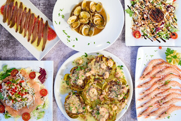 White marble table with typical Spanish food. Grilled white prawns, Cantabrian anchovies, clams, eel salad and artichokes with ham