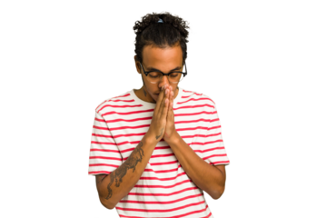 Young African American man isolated praying, showing devotion, religious person looking for divine inspiration.