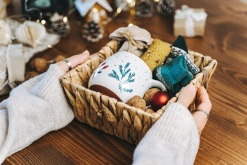 Woman s hands wrapping Christmas eco gift wicker basket, close up. Unprepared presents on wooden...