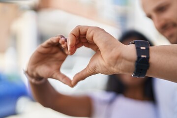 Man and woman interracial couple doing heart gesture with hands at street