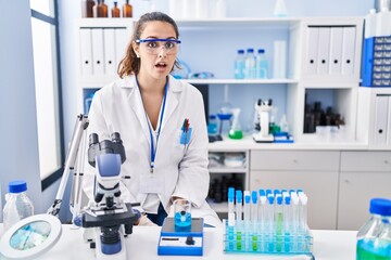 Fototapeta premium Young hispanic woman working at scientist laboratory afraid and shocked with surprise expression, fear and excited face.