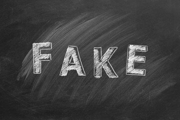 The word FAKE written in chalk on a blackboard. Information and disinformation concept. Fake news. Hand drawn illustration.