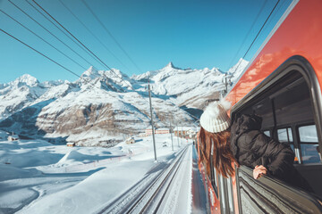 Happy woman traveler looks out from window traveling by train in beautiful winter mountains, Travel...