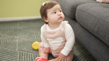 Adorable toddler sitting on floor with serious expression at home