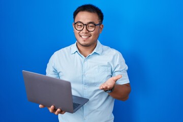 Chinese young man using computer laptop pointing aside with hands open palms showing copy space,...