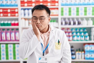 Chinese young man working at pharmacy drugstore thinking looking tired and bored with depression problems with crossed arms.