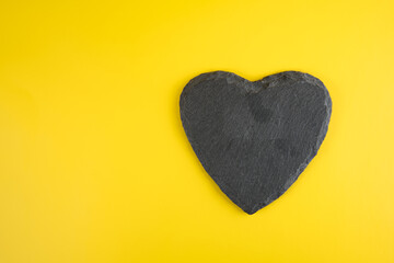 natural welsh slate mined and carved heart shaped drinks coaster isolated against a yellow background