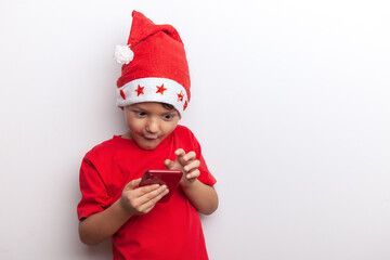 a boy in a Santa costume holds a smartphone in his hands. an emotional little santa. a cheerful child for Christmas with a phone.
