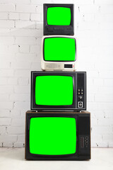 Four vintage green screen televisions with a white brick background.