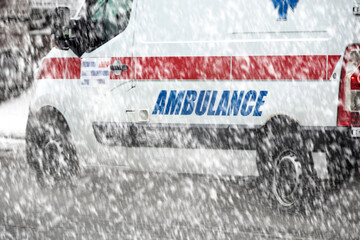 911 ambulance van rushing through traffic during heavy winter snowfall conditions. © astrosystem