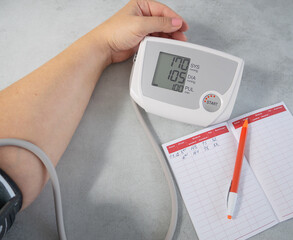 A woman measures blood pressure, pulse and writes down the readings in a notebook on a gray...