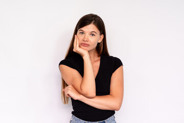 Portrait of bored young woman looking at camera over white background. Indifferent Caucasian lady wearing black T-shirt and jeans leaning head on hand. Boredom concept